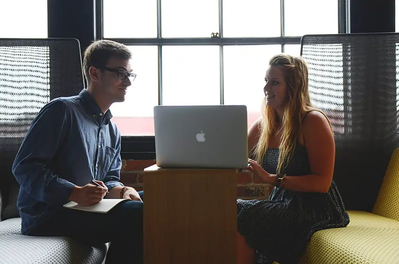 Two people talking while in front of a laptop