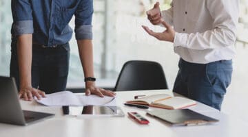 two people having a discussion next to a white desk – looking at a paper report