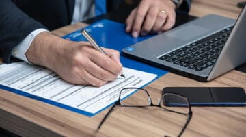 A lawyer writing in a paper while in front of laptop