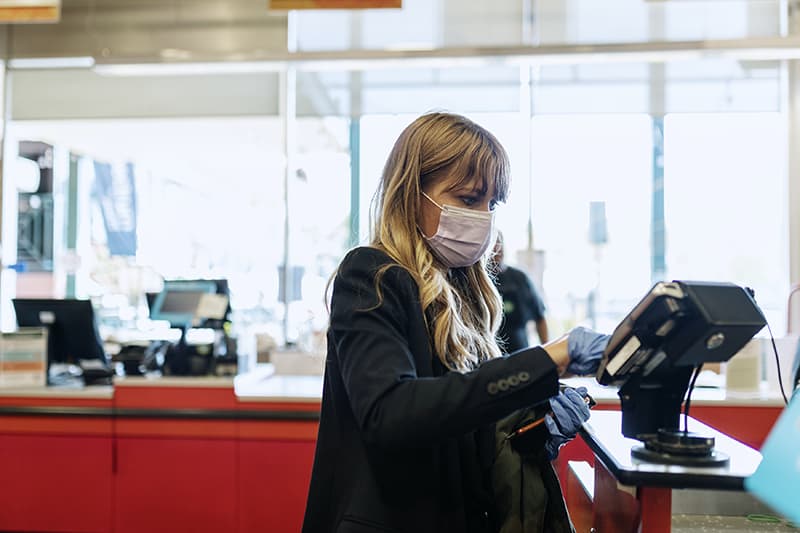 Woman in a face mask wearing latex gloves while purchasing at a self-checkout in a supermarket