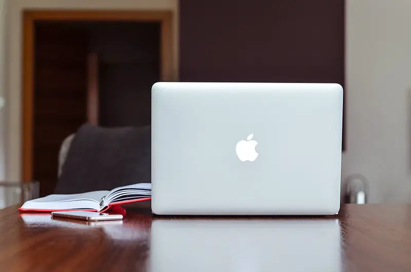 Silver macbook on the table beside the notebook