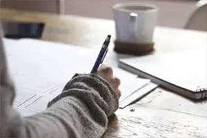 Person writing on a white paper beside the white cup