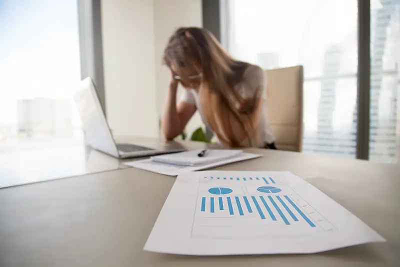 Depressed frustrated businesswoman holding head in hands, female boss shocked by decreasing sales in documents, focus on falling stats, profit loss graphs, company bankruptcy or financial problems