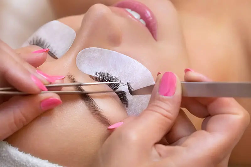 Beautiful Woman with long eyelashes in a beauty salon. Eyelash extension procedure by Eyelash Artist Entrepreneur. Lashes close up.