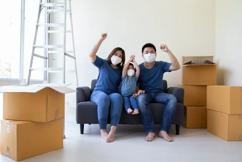 Family wearing masks sitting on sofa next to packed boxes in new home