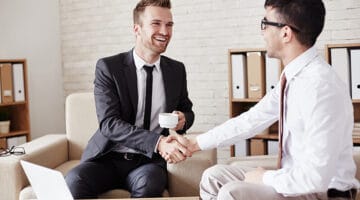 Business partners in formalwear greeting one another in office