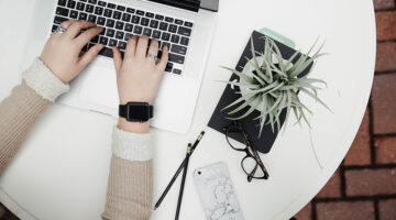 Person typing on a laptop next to a plant
