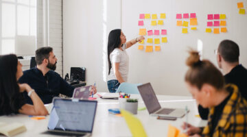 woman placing sticky notes on wall in business meeting