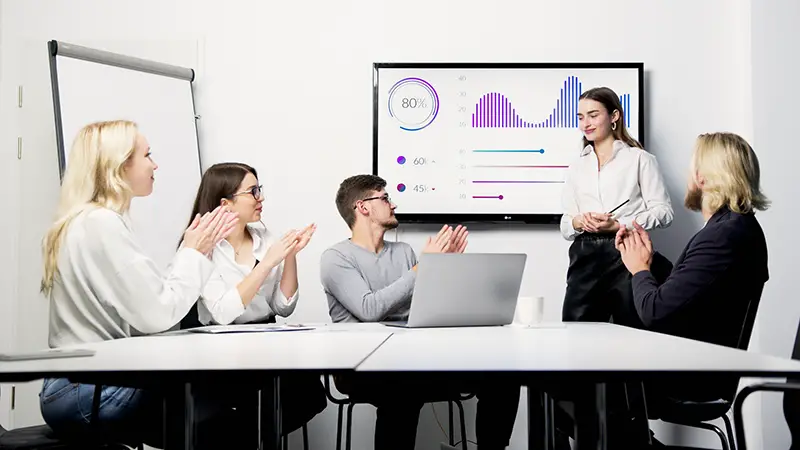Woman in front of her colleagues showing a graph in a white board