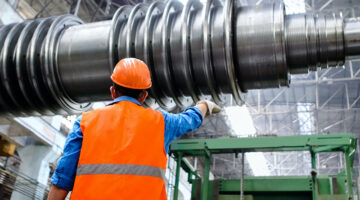 Man wearing orange hard hat and high visibility vest while inspecting equipment