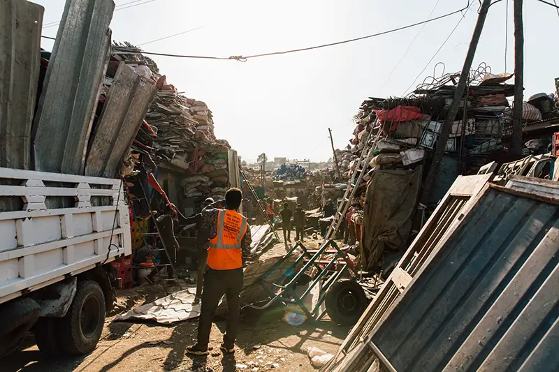 Worker standing near pile of metal scrap in dump