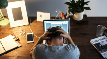Man holding his head while in front of his laptop