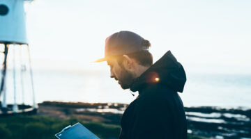 Young man wearing black jacket and cap near seaside