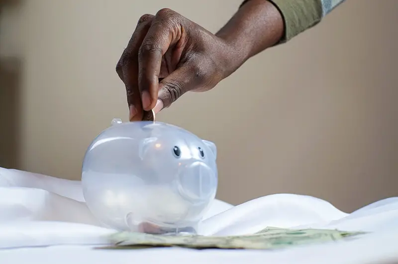 Person putting coin into plastic piggy bank