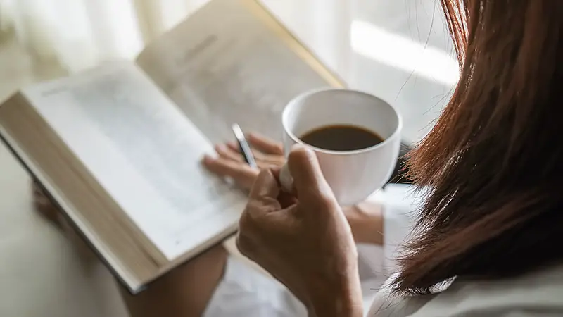 Woman holding coffee while reading
