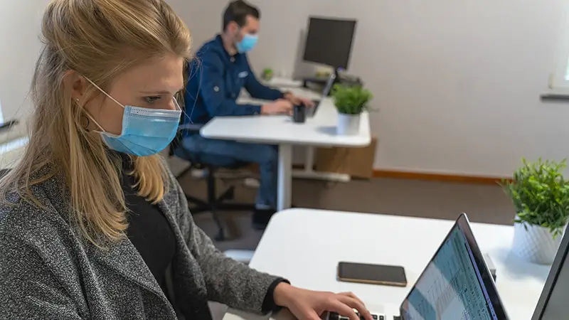 Woman and man wearing facemask working on laptop