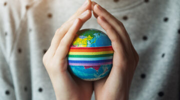 woman's hands holding globe with LGBT rainbow ribbon