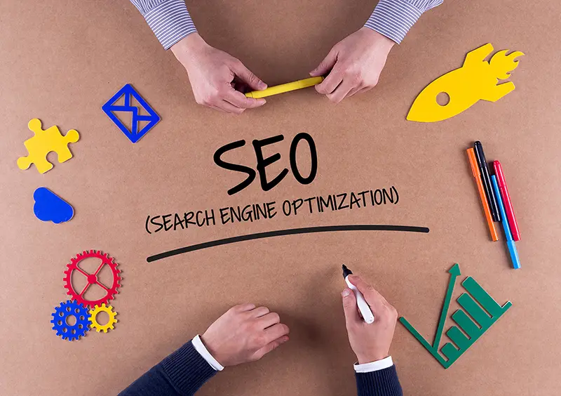 Two people holding pen with SEO text in the middle of brown board