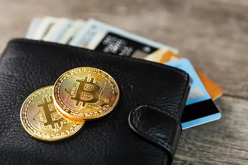 Black wallet with banknotes, electronic cards and bitcoins on a wooden background