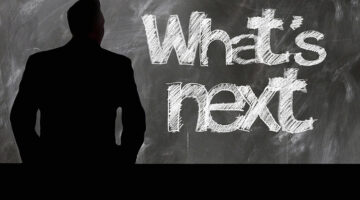 business man looking at a black board witht he words What's next written on it