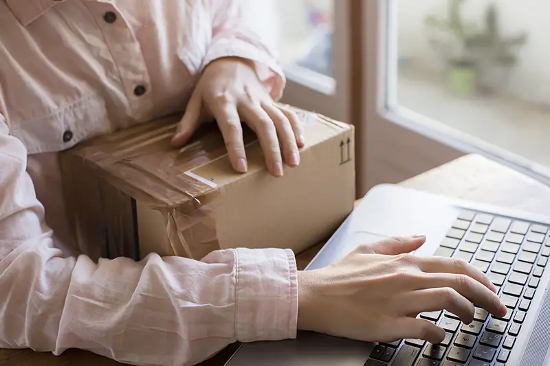 A close up of a female hand with a keyboard and a parcel, buying things on the internet