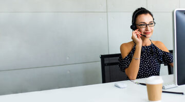 Beautiful consultant of call center in headphones. Portrait of smiling female customer using headset at call center office, VOIP
