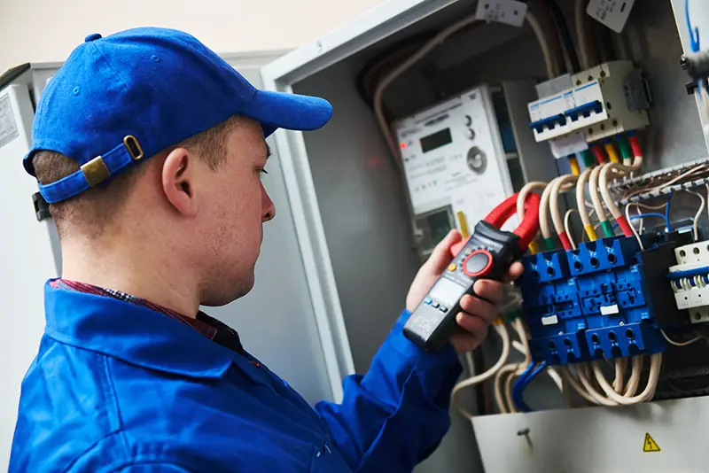 Electrician working while holding multimeter tester in switchbox