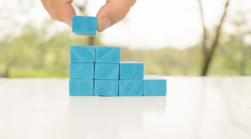 Man's hand holding blue wooden block on white wooden table.
