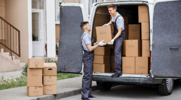 Two young handsome movers wearing uniforms are unloading removal van