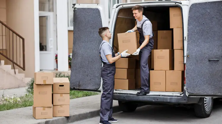 Two young handsome movers wearing uniforms are unloading removal van