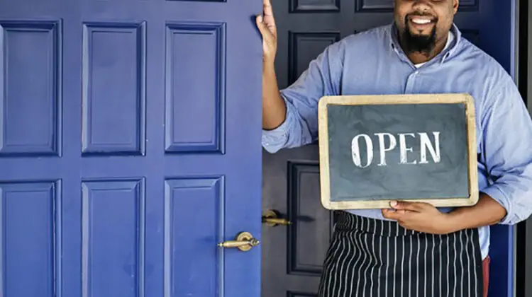 Man standing beside blue door holding open signage