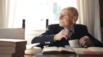 elderly gentleman drinking a hot beverage while sitting at a table with books