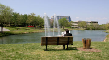 Person reading newspaper on bench in park near pond and fountain