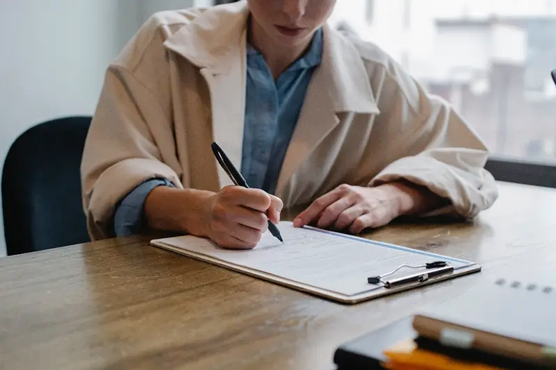 Woman writing on white paper in clipboard