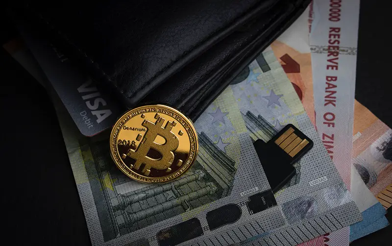 Bitcoin beside black wallet and paper bills