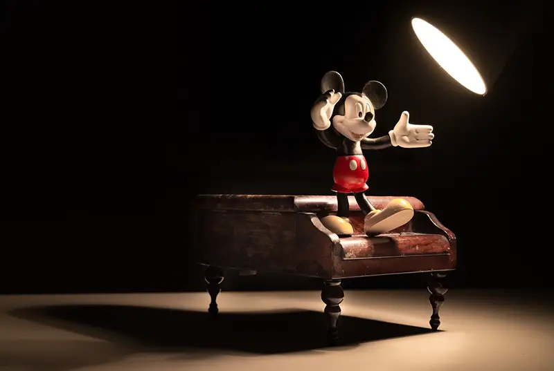 Micky mouse standing on a piano in the spotlight