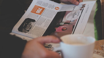 Person reading magazine while holding white ceramic mug