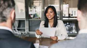 young asian woman smiling and holding resume, while sitting in front of directors during corporate meeting or job interview