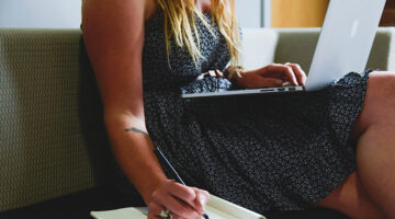 Entrepreneur making notes in notepad - laptop on lap