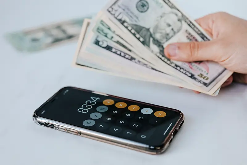 Person holding dollar bills near calculator