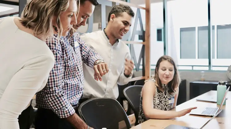 members of a team looking at a computer - three standing and one seated