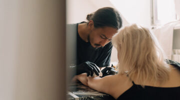 Man in black shirt putting tattoo in woman left arm