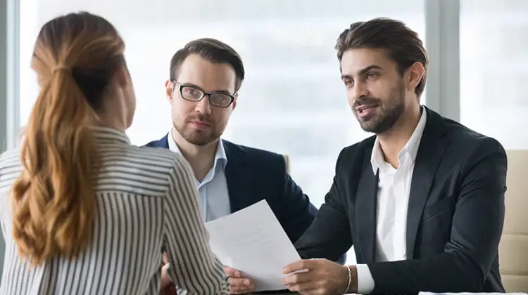 Two male hr managers at interview with female applicant. Man with resume in hands asks questions to candidate. Hiring, staff recruiting process.