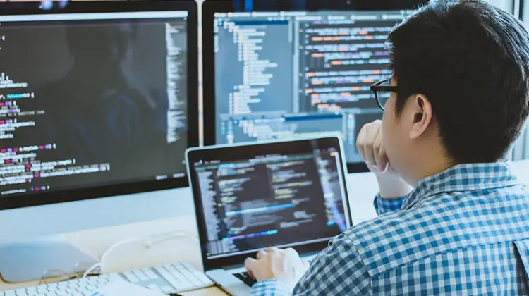 IT specialist in front of computer screen and laptop