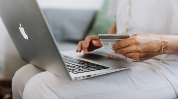 Person using MacBook and holding credit card