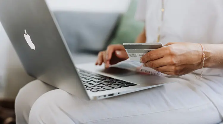 Person using MacBook and holding credit card