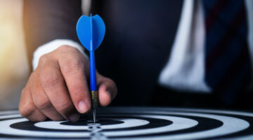 Businessman holding blue dart pin pointing to dartboard