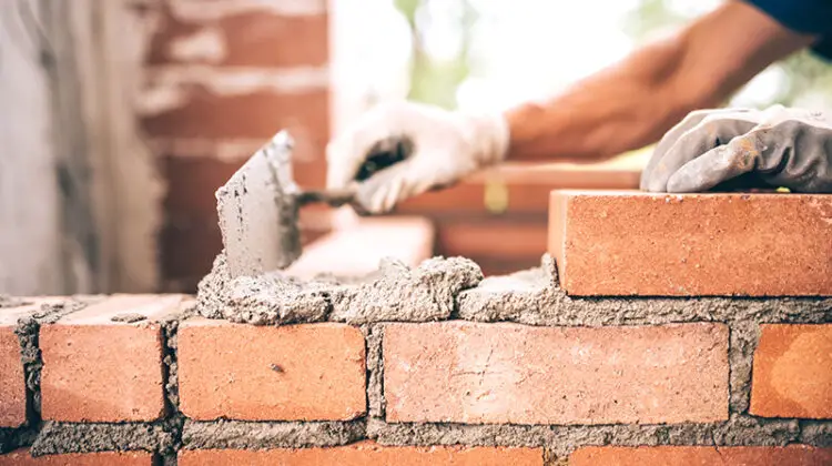 Bricklayer worker installing brick masonry on exterior wall