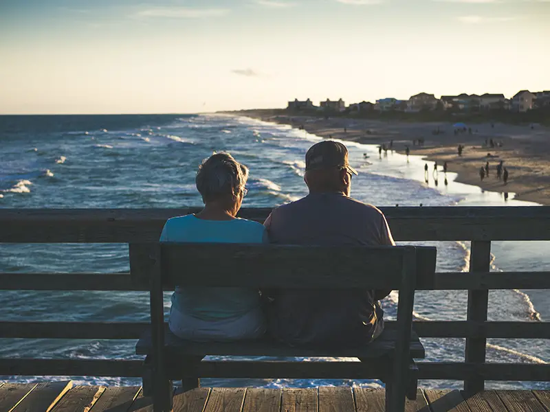 man and woman sitting on the bench in front of beach