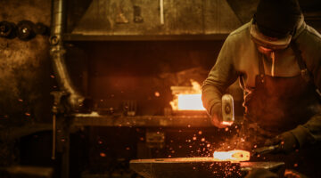 The blacksmith forging the molten metal on the anvil in smithy.